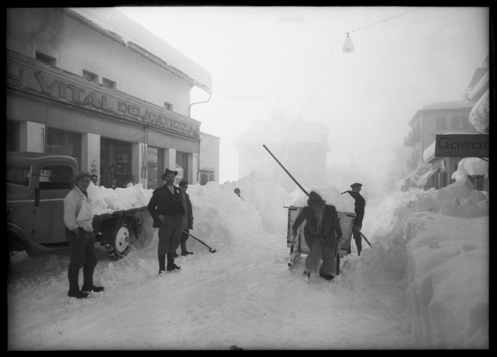 Schneeräumung in Scuol, Unterengadin. Zum Einsatz kommen Motorlastwagen und Schlitten (Aufnahme ca. 1930er Jahre). Signatur: Staatsarchiv Graubünden N1.L-4266-NG, Schneeräumung Scuol, 1930er Jahre, Fotograf: Johann Feuerstein (Scuol).